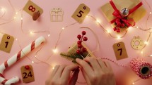 Girl's hands creating paper Christmas gift on the pink table