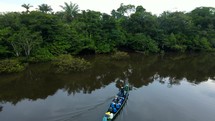 Aerial shot drone pans right around canoe boat on black lagoon in middle of Amazon rainforest just before sunset as it approaches the shore