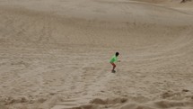 Young boy sandboarding down dune hill in front of beach on summer day - rack focus - visualization success