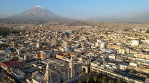 Aerial shot drone flies up and away from the Arequipa Cathedral and Plaza de Armas with the Misti Volcano in the distance at dusk