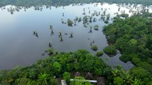 Aerial shot drone flies over indigenous village next to black lagoon in middle of Amazon rainforest just before sunset