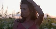 Attractive woman in 20s holds hair up as she looks towards camera - outdoors at sunset - medium shot