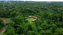 Aerial shot drone flies toward lodge on brown river in middle of Amazon rainforest in establishing shot