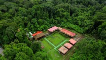 Aerial shot drone flies toward lodge on brown river in middle of Amazon rainforest in establishing medium shot