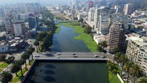 Aerial shot drone flies backwards over river with two bridges crossing it with city in the background