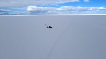 Aerial shot drone flies forward in super wide shot of jeep on the salt flats in the middle of the day with no one else in sight