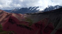 Aerial shot drone flies backwards from red and gray mountain with snow capped mountains in the background