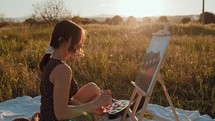 Young girl paints the picture on canvas in the countryside