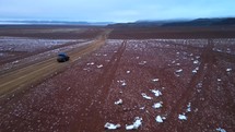 Aerial shot drone flies low to the right of jeep along snow covered red desert