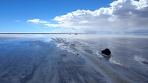 Aerial shot drone flies to left as it passes jeep driving on salt flats on cloudy day