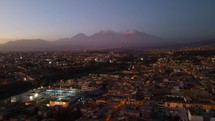 Aerial shot drone flies over lit up highway in Arequipa at sunset toward Chachani Volcano
