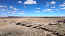 Aerial shot drone orbits to right around train cemetery in desert on sunny day with blue skies as clouds roll through the frame