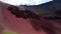 Aerial shot drone slowly flies left in front of rock formation on red mountain as clouds cast shadows