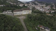 Drone orbits the left around the backside of Church of Saint Francis of Paola overlooking the town of Ouro Preto and its hills and valleys