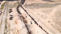 Aerial shot drone orbits to left in wide shot around train cemetery in desert