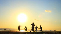 teen boys playing soccer on the beach at sunset 