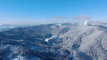 Vista Of Dense Woodland On Snow Mountains During Winter Season. Aerial Drone Pullback