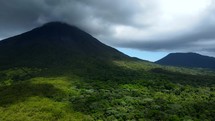 Aerial shot drone flies up and toward cloud-covered volcano in middle of lush green forest