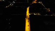 Aerial shot drone flies backward over well lit street in downtown Quito at night
