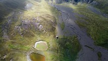 Aerial shot drone flies backwards facing sun over two ponds reflecting the clouds above