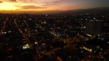 Aerial shot drone flies to right as camera slowly pans left revealing the city at sunset