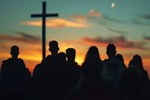 Silhouettes of a group of people with a cross in the background at sunset