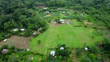 Aerial shot drone flying over open green field of indigenous village in middle of Amazon rainforest.