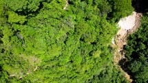 Aerial shot drone flies to right with camera facing down over top a jungle to reveal a large waterfall and pool