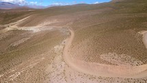 Aerial shot drone flies forward over desert road and follows it toward the mountains