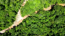 Aerial shot drone slowly ascends and spirals with camera facing down over a jungle with a small river running through it