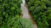 Aerial shot drone flies over and away from lodge on brown river in middle of Amazon rainforest