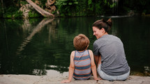 a mother and son sitting on a river bank