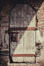 Old wooden door or window in a stone wall with rusted metal straps and lock, 