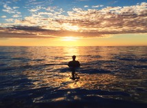 man standing in ocean water at sunset 
