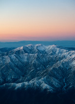 View from a plane going over a scenic mountain range with the sun setting behind. 