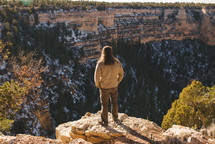 man standing on the edge of a cliff looking down 