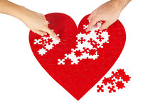 Young couple assembling a red puzzle heart shape on white background.