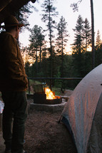 man standing near a tent and campfire 