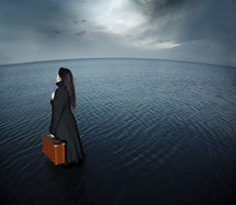 a woman holding a suitcase standing in water 