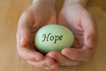 Hands cradling a green egg reading, "hope."
