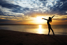 a woman dancing on a beach at sunset 