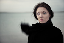 a woman in a black coat and scarf standing on a lake shore 