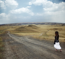 a woman walking down a dirt road 