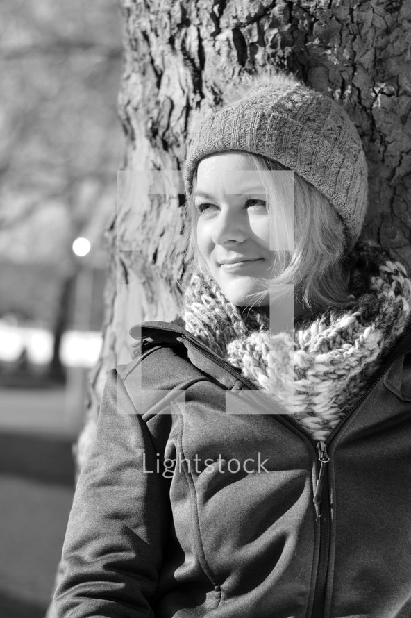 portrait of a young woman leaning against a tree smiling 