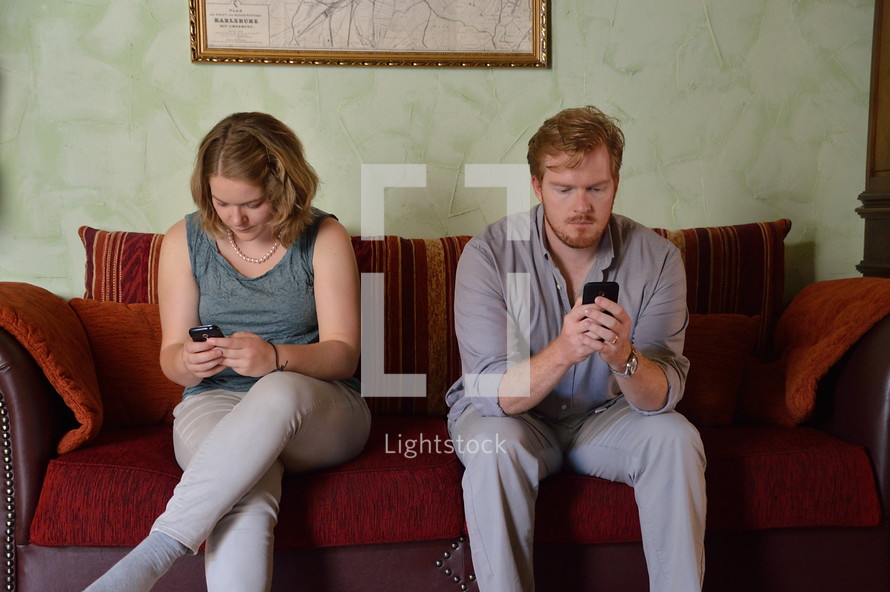 couple sitting on a couch looking at cellphones 