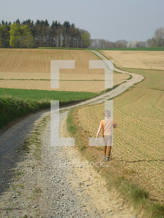 Child walking along a winding road through the countryside.
