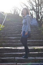 young woman looking back and going up a stairway that is leading to the light. 
