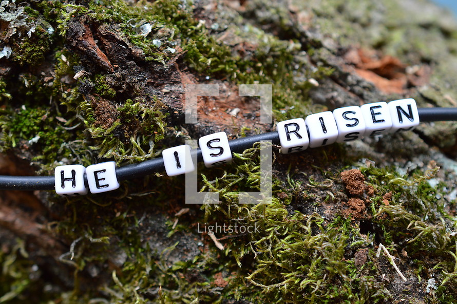 He Is Risen beads on a bracelet on a mossy log 