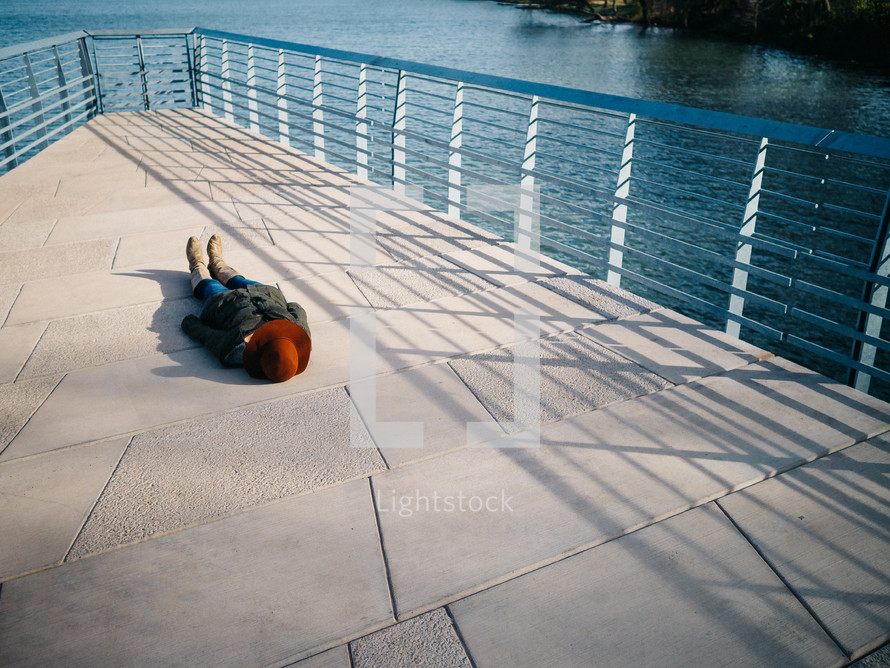 A woman lays on a dock over a lake.