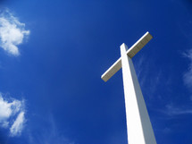 The glory of The Cross. A white cross stretches out to Heaven against a bright and blue sky towering above the clouds and the world to reveal the hope and glory of Jesus Christ. 